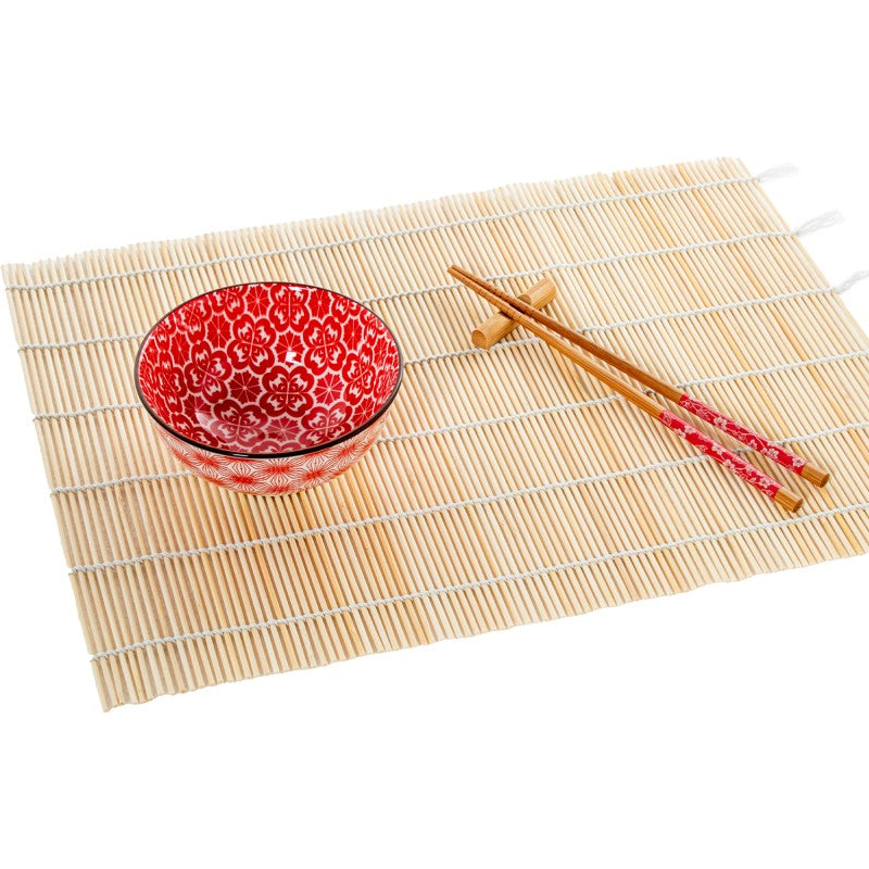 Cuenco de porcelana con diseño floral rojo sobre salvamanteles de bambú, acompañado de palillos