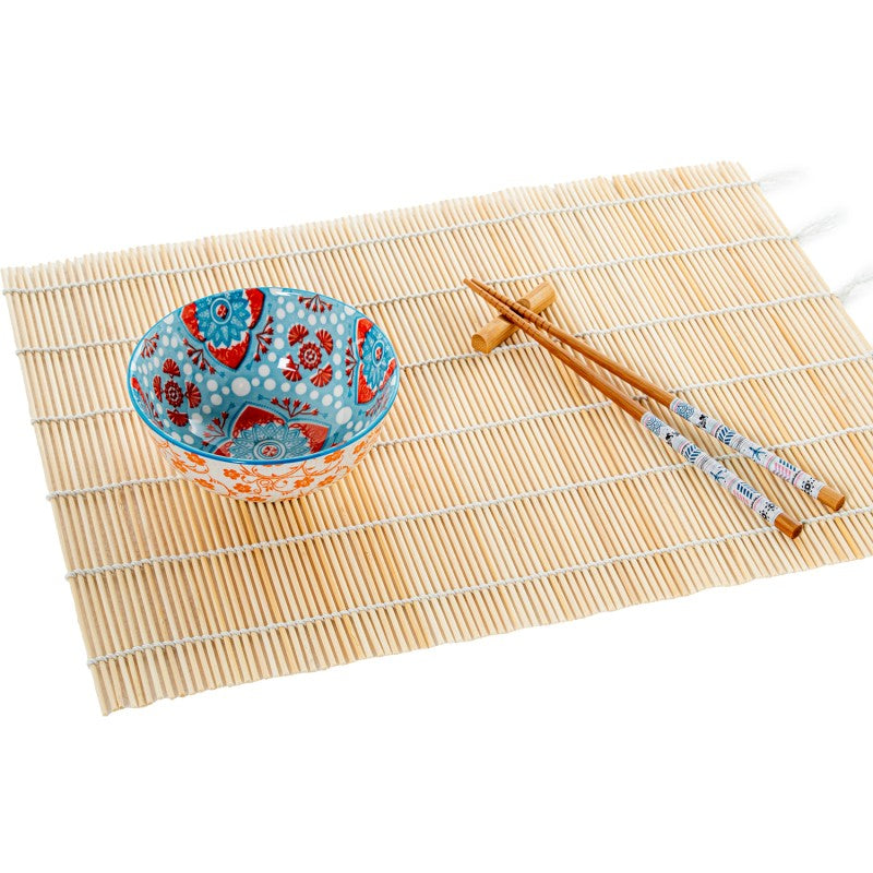 Cuenco de porcelana con diseño floral azul y naranja de estilo oriental sobre salvamanteles de bambú, acompañado de palillos