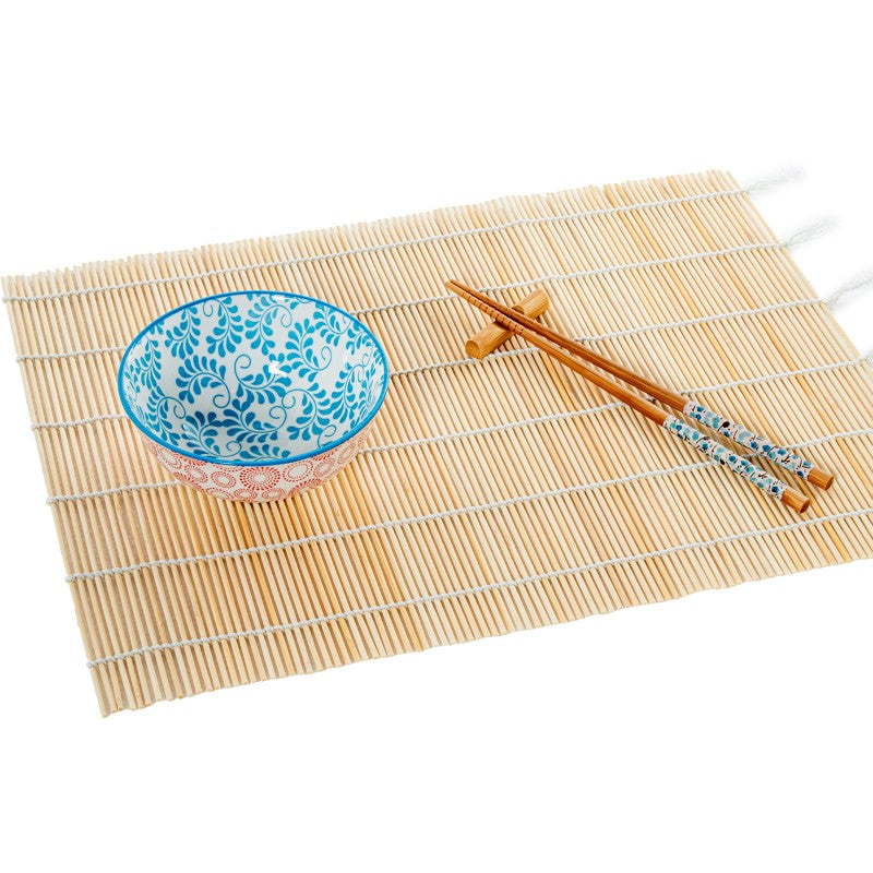 Cuenco de porcelana con diseño floral azul sobre salvamanteles de bambú, acompañado de palillos