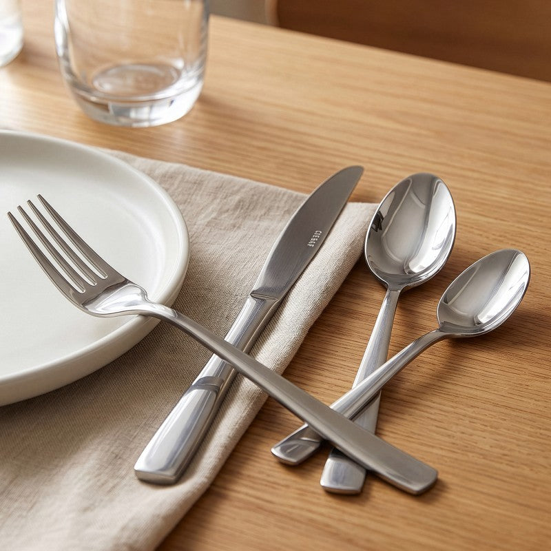 Mesa puesta con el set de cubiertos Lucia plata brillante sobre madera clara, plato blanco, servilleta y copa de vidrio