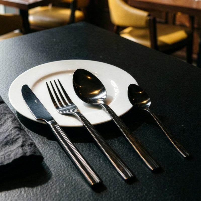 Mesa puesta en ambiente de restaurante con el set de cubiertos Alba sobre plato de cerámica blanca y mantel oscuro
