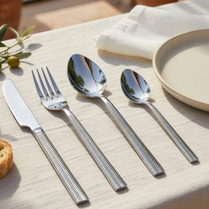 Mesa puesta con el set de cubiertos Alba plateado sobre mantel de lino, servilleta y plato de cerámica, ambientación elegante