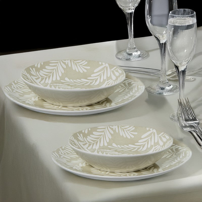 Vajilla de porcelana beige con hojas blancas dispuesta en mesa elegante junto a copas de cristal