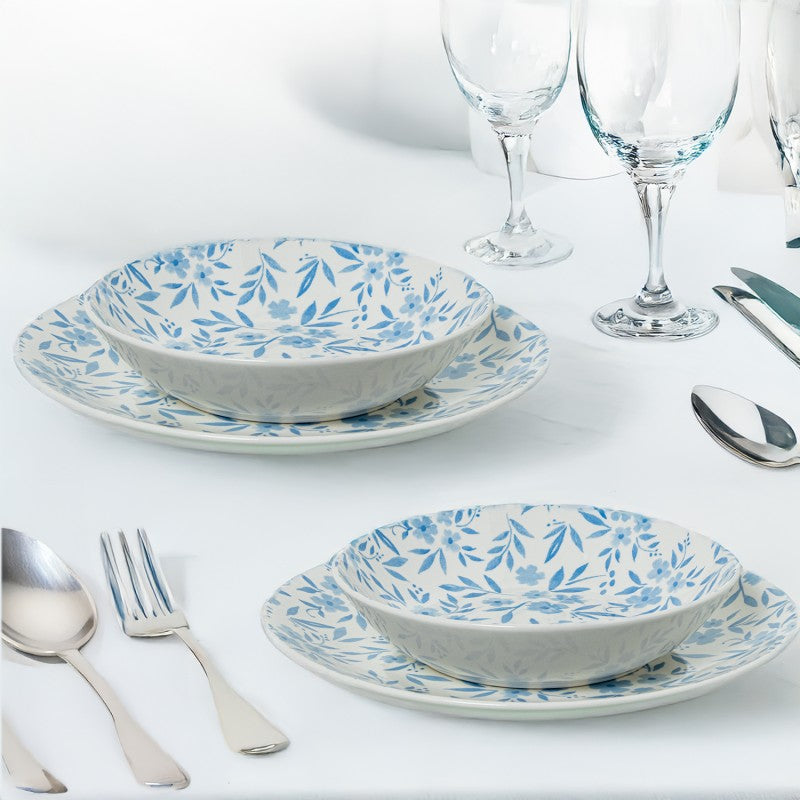 Plato y tazón de porcelana con flores azules dispuestos en mesa junto a copas y cubiertos