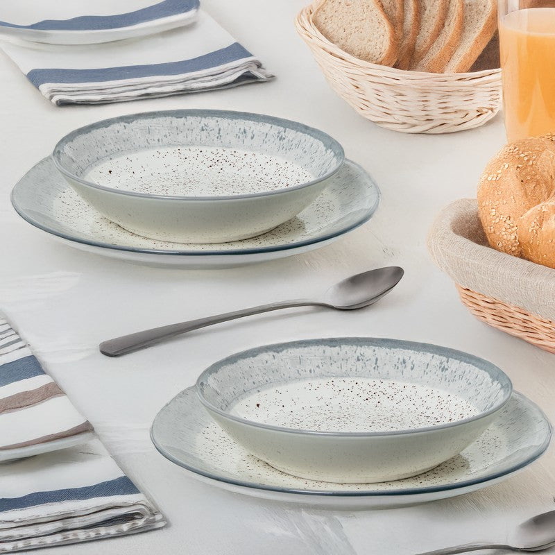 Platos hondos de porcelana con acabado moteado gris servidos en mesa junto a pan y zumo de naranja