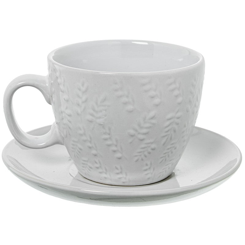 Detalle de una taza de té de cerámica blanca con plato, mostrando el relieve floral delicado en la superficie