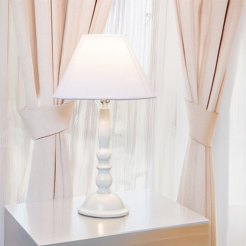 Lámpara de sobremesa blanca sobre mesita junto a cortinas de gasa en tono rosa palo
