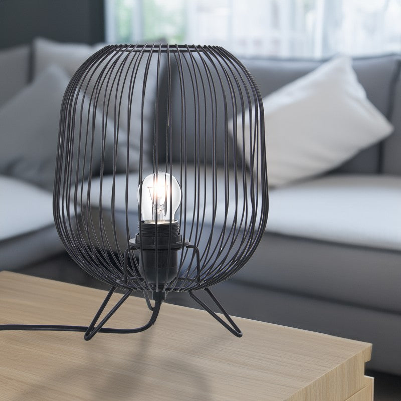Lámpara de sobremesa de metal negro encendida sobre mesa auxiliar junto a sofá en salón