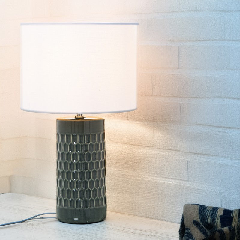 Lámpara de sobremesa encendida junto a una pared de ladrillo blanco, ambiente rústico y cálido