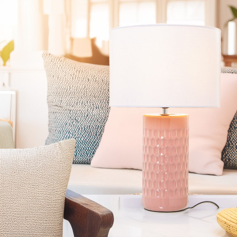 Lámpara de sobremesa cerámica rosa decorando un salón junto a cojines en tonos rosados y beige