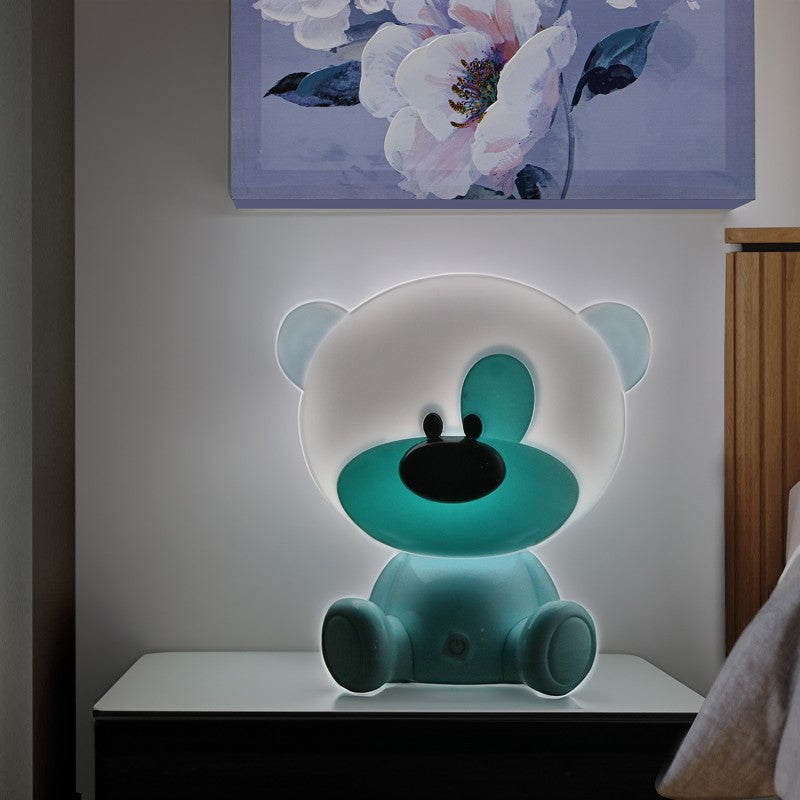 Lámpara osito azul encendida decorando una mesita junto a un cuadro floral