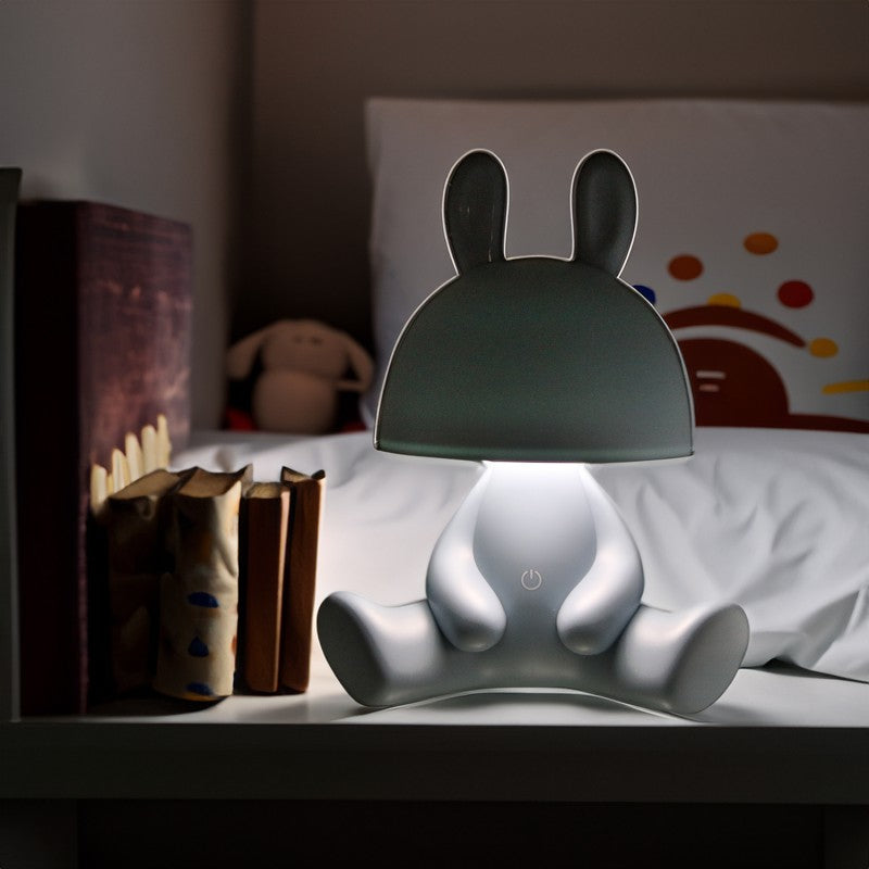 Lámpara conejo azul encendida decorando una mesita de noche junto a libros