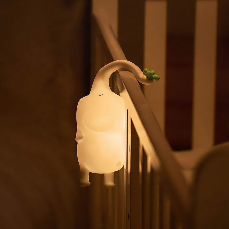 Luz nocturna de elefante encendida, colgada con su trompa en una barandilla de escalera