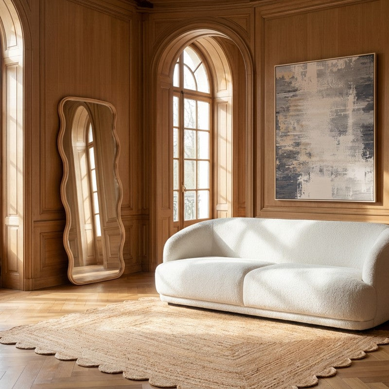 Espejo ondulado de madera apoyado en el suelo, decorando un salón con paneles de madera y sofá blanco