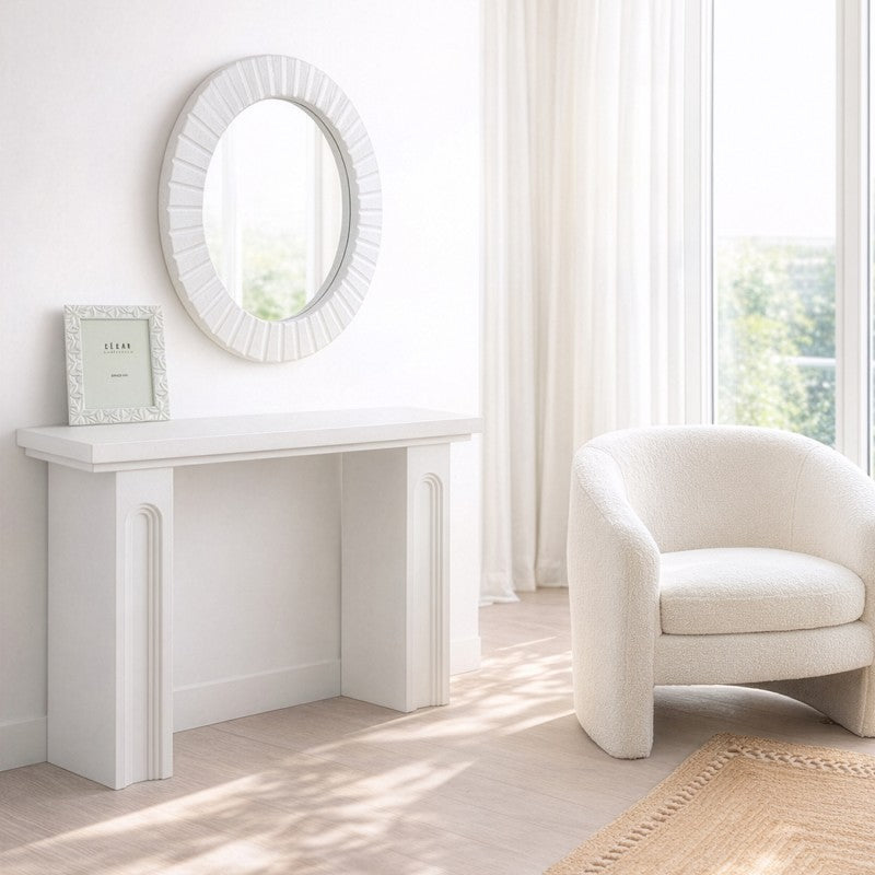 Espejo redondo blanco decorando un recibidor junto a consola y sillón en tonos claros