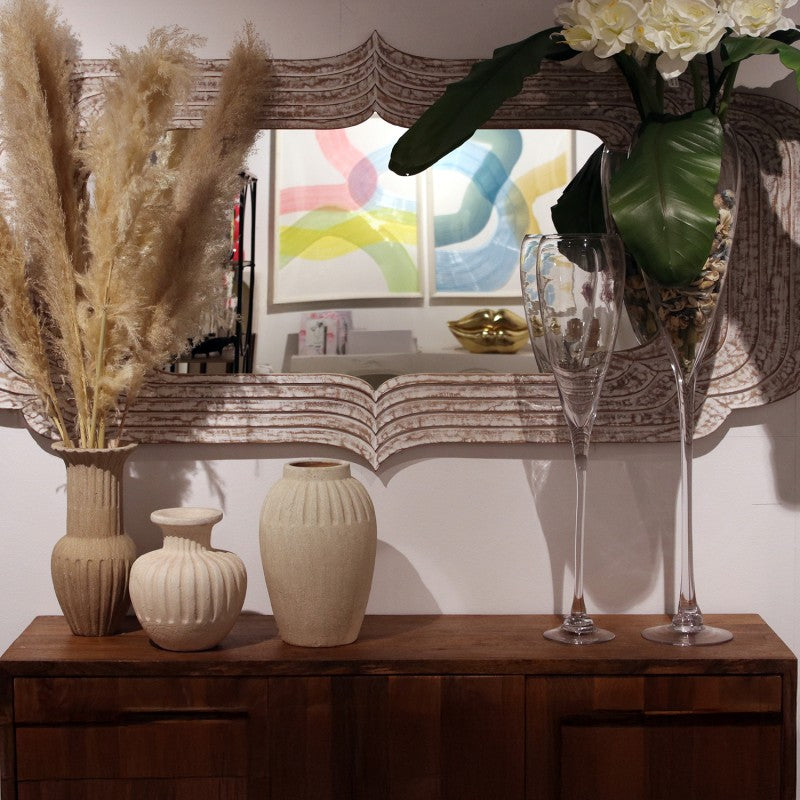 Espejo de madera de mango sobre un mueble de madera oscura con jarrones y copas decorativas