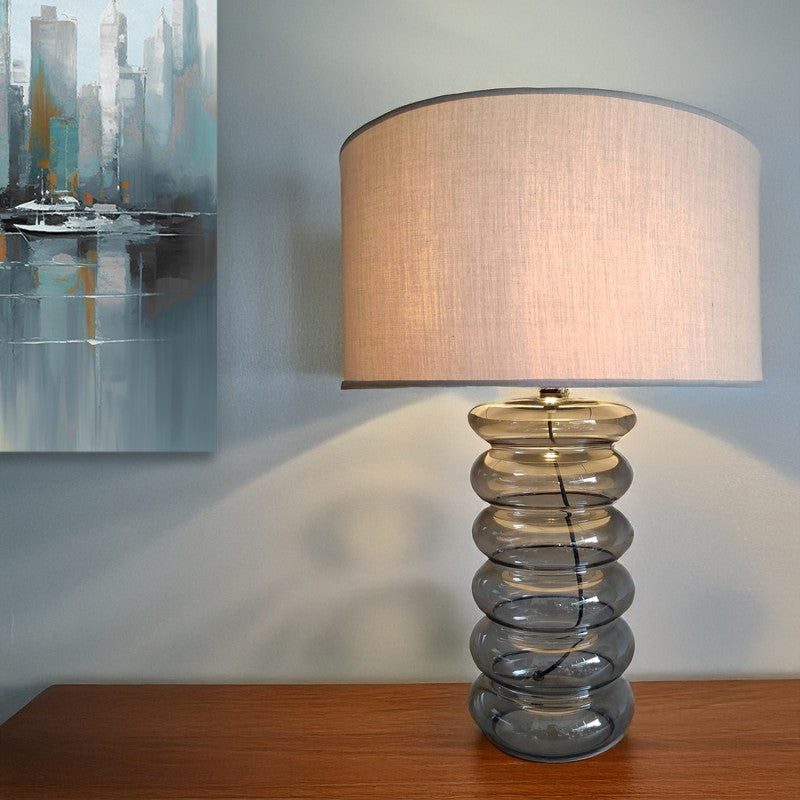 Lámpara de cristal encendida sobre mesa de madera junto a un cuadro moderno